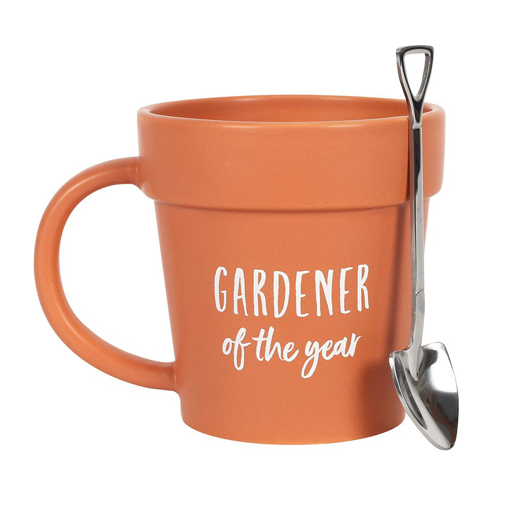 A terracotta style plant pot shaped mug featuring white text saying 'Gardener of the Year' on the front and a matching shovel shaped spoon.