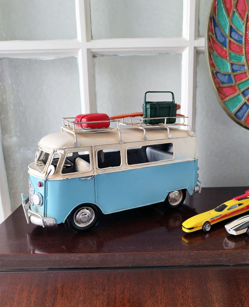 An image of a metal ornament in the shape of a blue 60s camper van with vintage luggage on the roof.